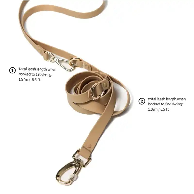 A sand colored silicone coated webbing dog leash with a gold metal D-ring and a buckle showing leash length
