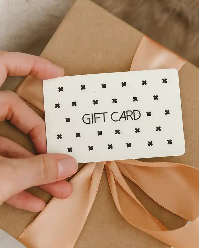 Hand holding a MiAmore gift card over a wrapped present with a beige ribbon.