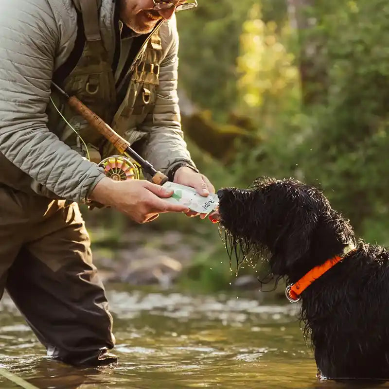 Person in outdoor gear feeding a dog Rigby pouch in a river
