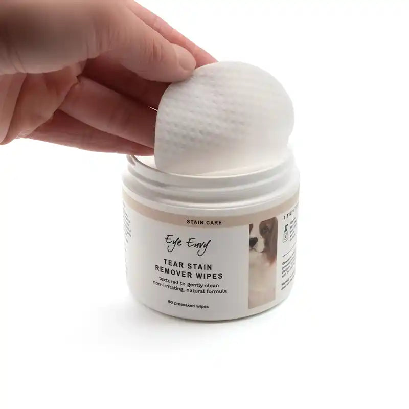 Hand reaching into a jar of 'Eye Envy' tear stain remover wipes on a white background