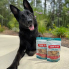 Black dog sitting next to two bags of Farm to Pet Fish Chips.