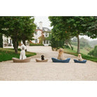 Four dogs sitting on enid blythe beds in a driveway with a large house in the background.