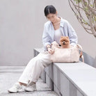 Woman sitting on a bench with cloud carrier next to her and pomeranian in the bag