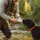 Person in outdoor gear feeding a dog Rigby pouch in a river