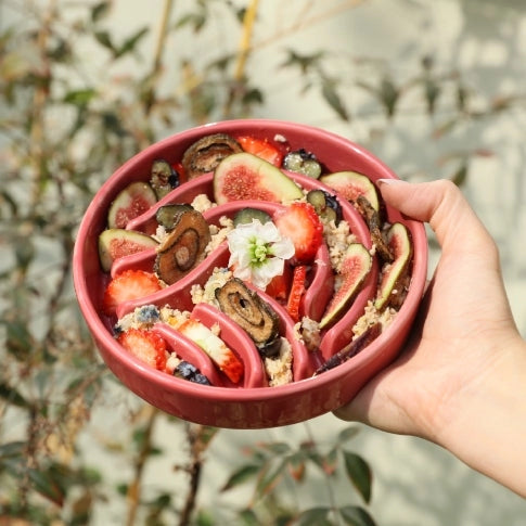 Hand holding a pink slow feeder bowl filled with a colorful salad against a natural background