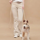 Woman wearing beige pants and white shoes holding tan rover leash with a schnauzer dog secured 